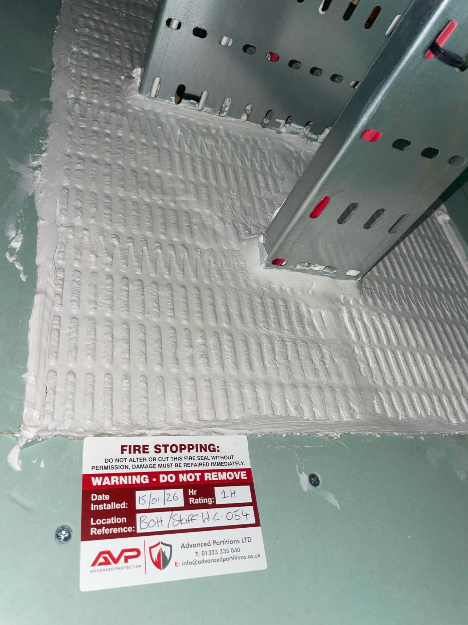 Two metal cable trays passing through a sealed wall opening with a firestopping label