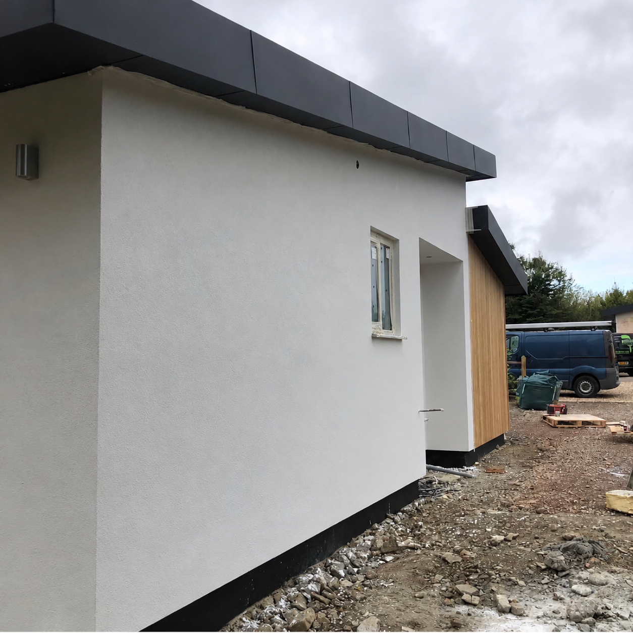 White rendered external walls with dark roof trim and adjacent timber cladding